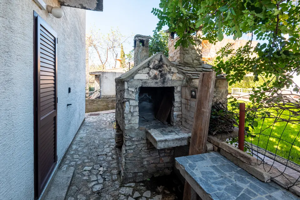Stone outdoor fireplace and barbecue in the shaded courtyard, under a vine